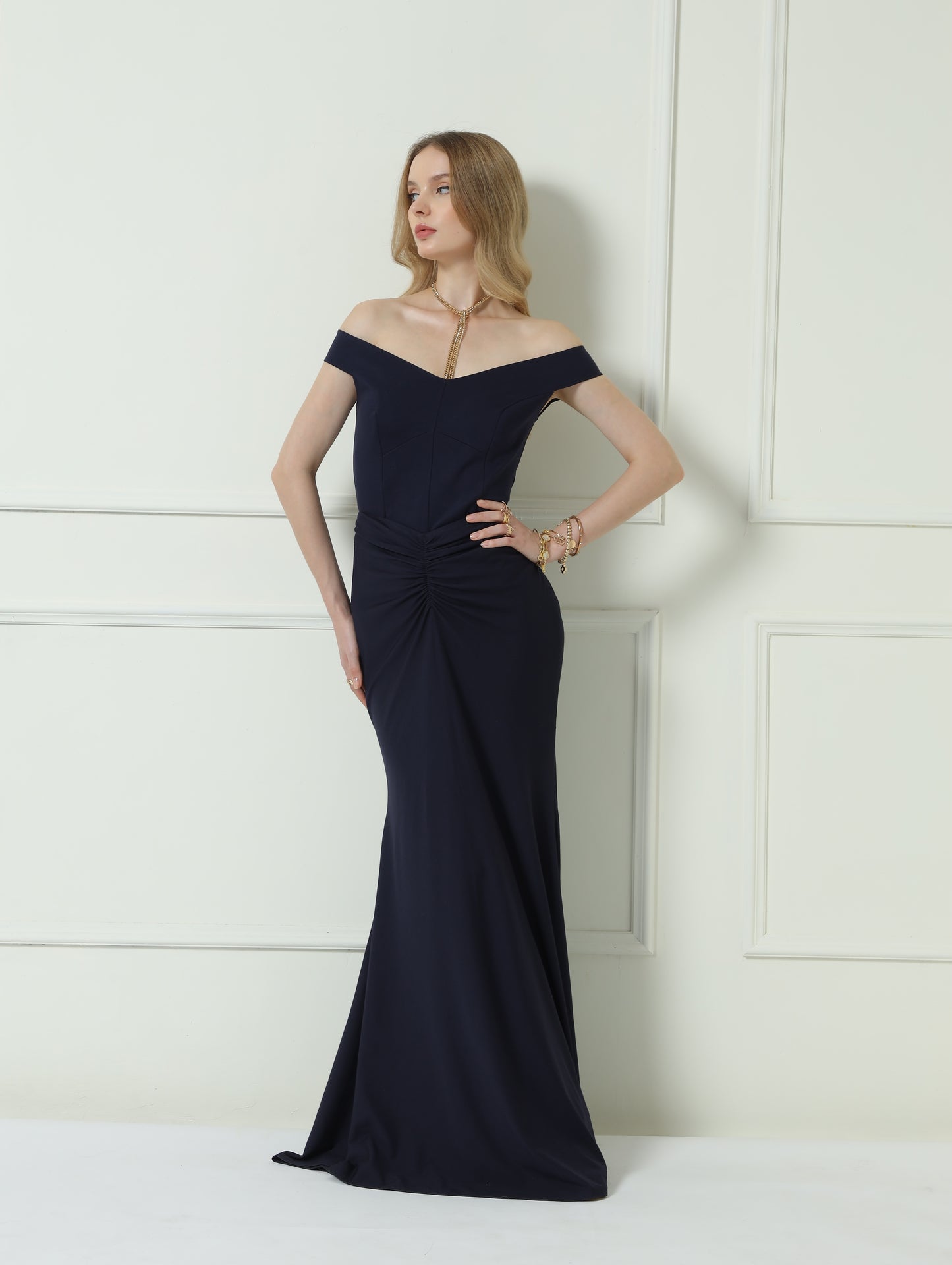 Woman wearing a black off-shoulder evening gown against a white wall