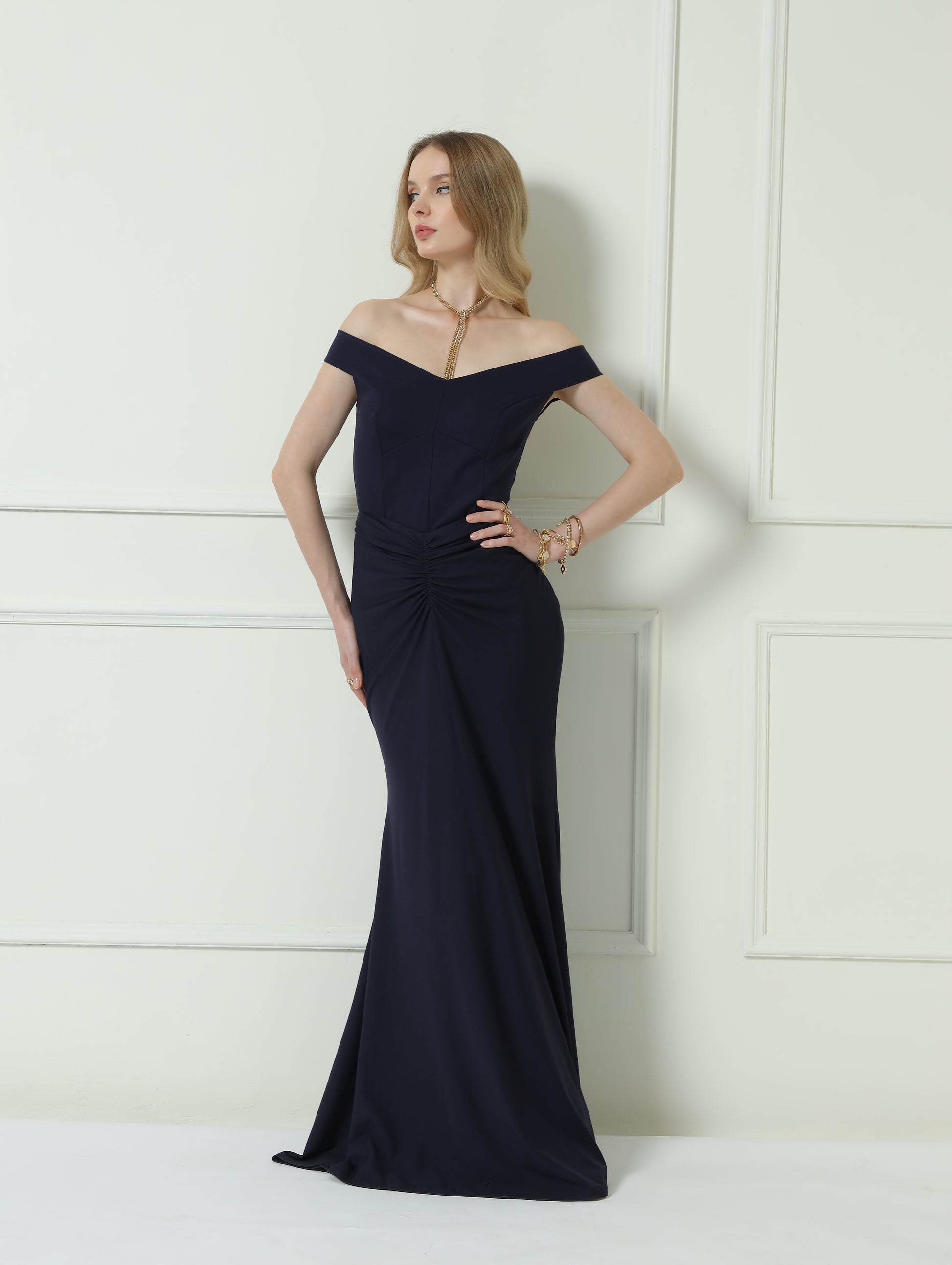 Woman wearing a black off-shoulder evening gown against a white wall