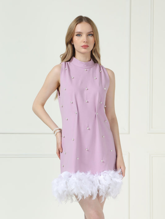 Woman wearing a light pink dress with white feather details against a white background