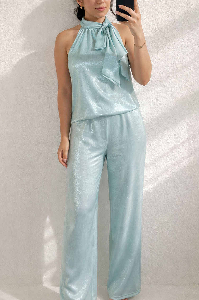 Woman wearing a light blue satin outfit taking a mirror selfie against a white wall.