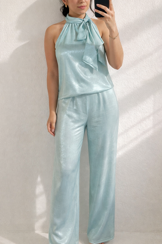 Woman wearing a light blue satin outfit taking a mirror selfie against a white wall.