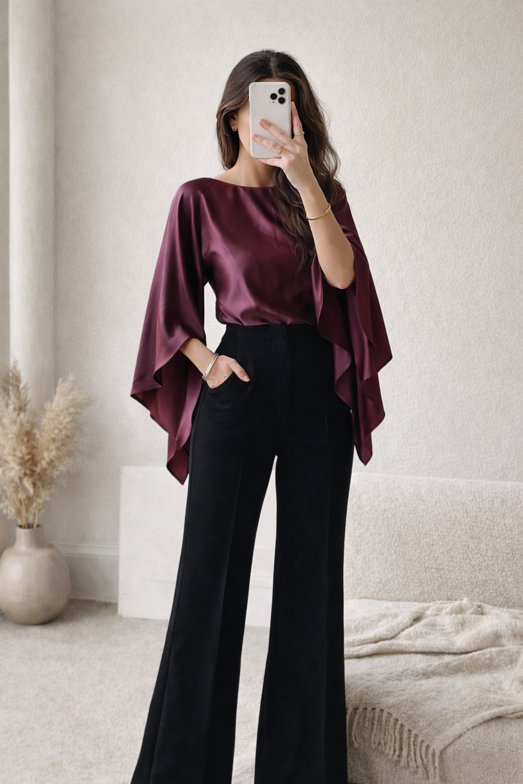 Woman wearing a burgundy top and black pants taking a mirror selfie.
